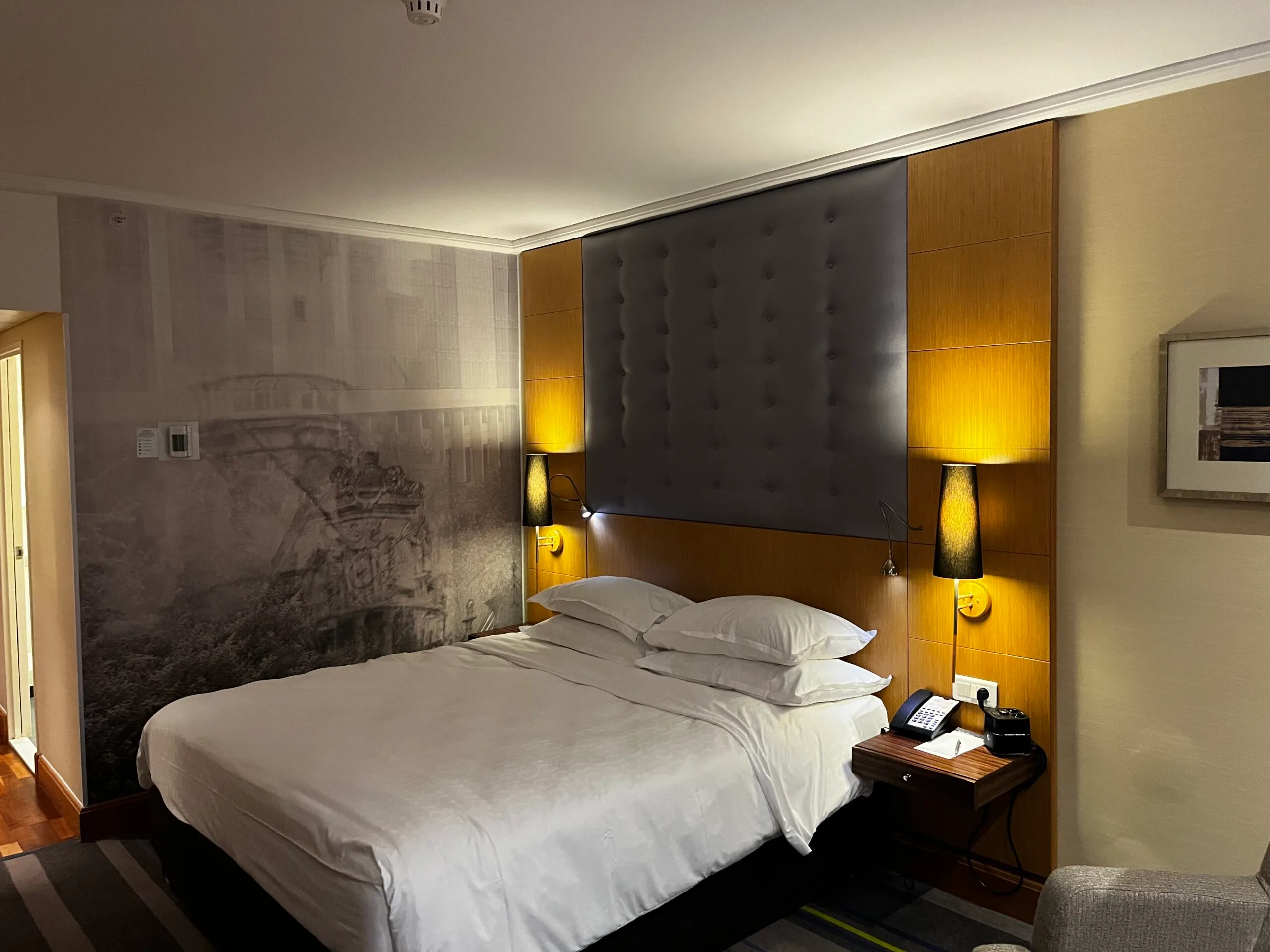 Doppelbett im Hotelzimmer mit grauem Kopfteil und Wandbild