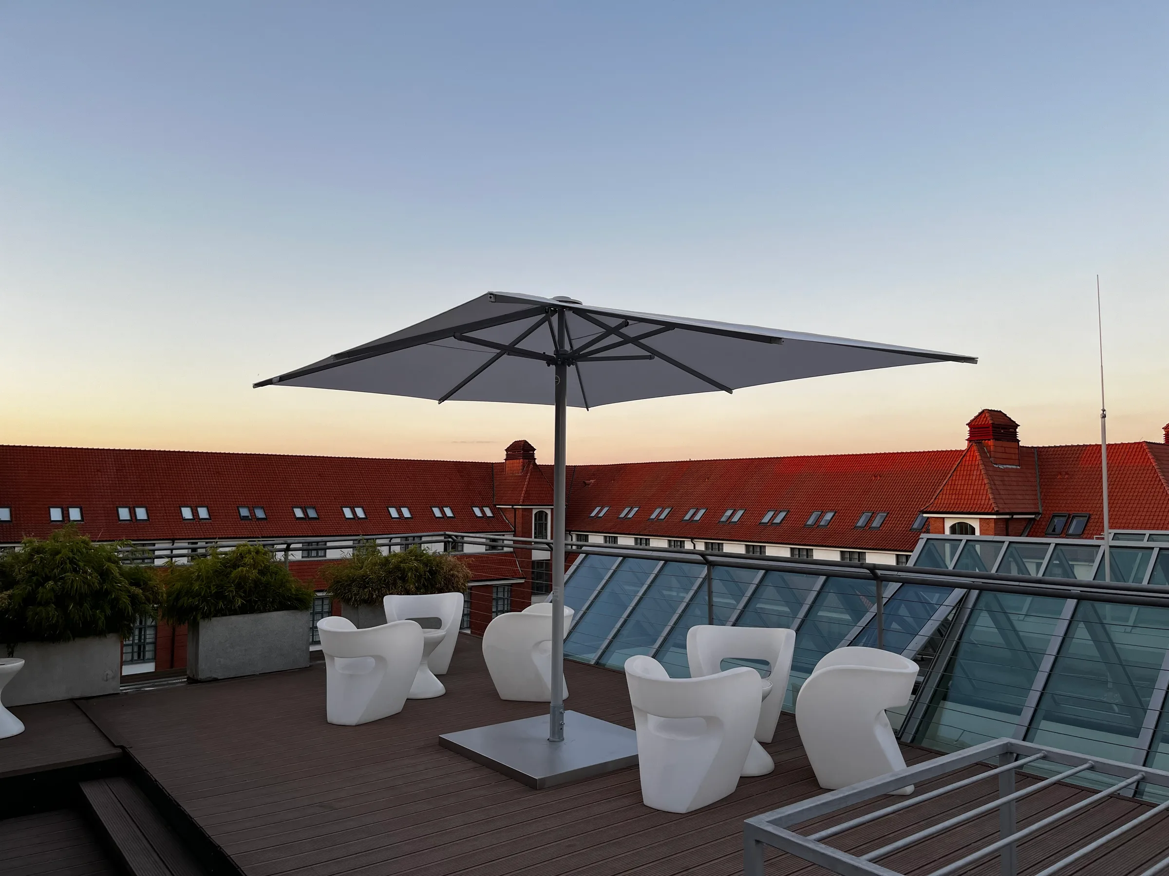 Dachterrasse mit Sonnenschirm und weißen Stühlen bei Sonnenuntergang