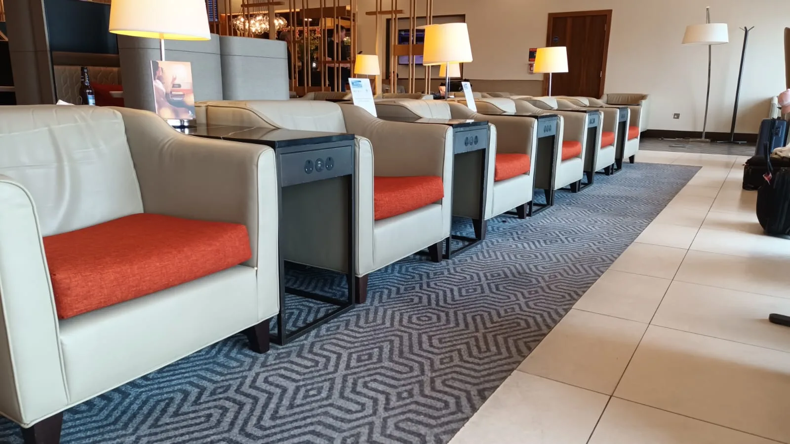 Reihen von Sesseln mit orangefarbenen Kissen in einem Flughafen-Lounge