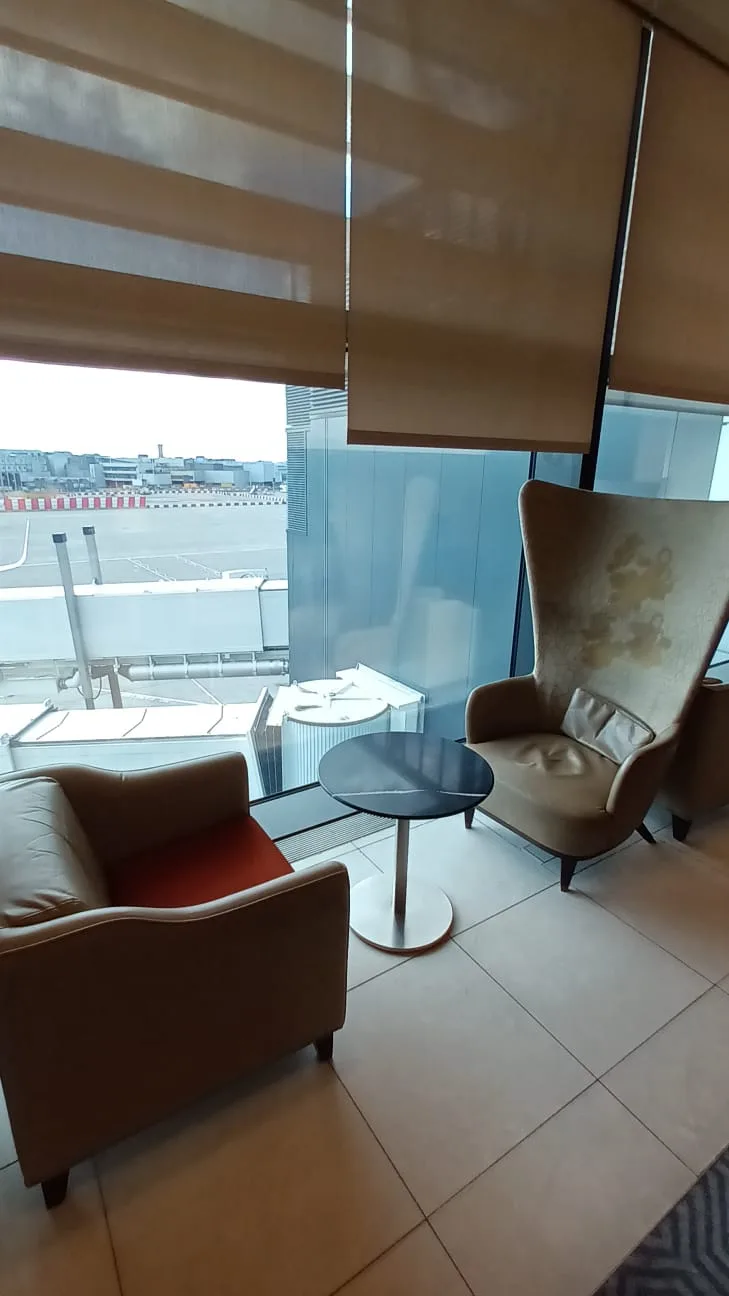 Lounge mit Sesseln und Tisch vor Fenster mit Flughafenblick