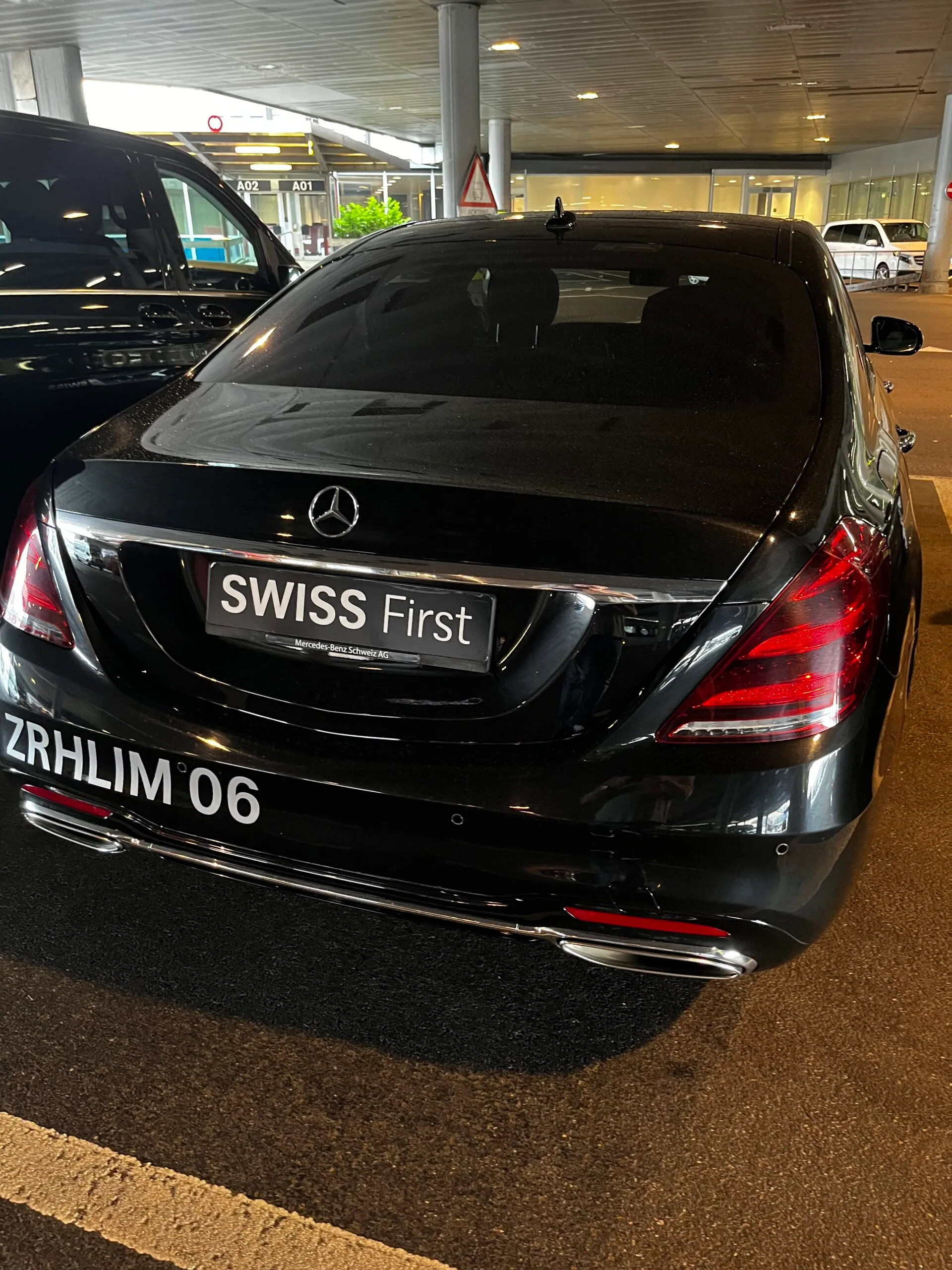 Schwarzer Mercedes-Benz mit 'SWISS First' Schild im Flughafenparkhaus