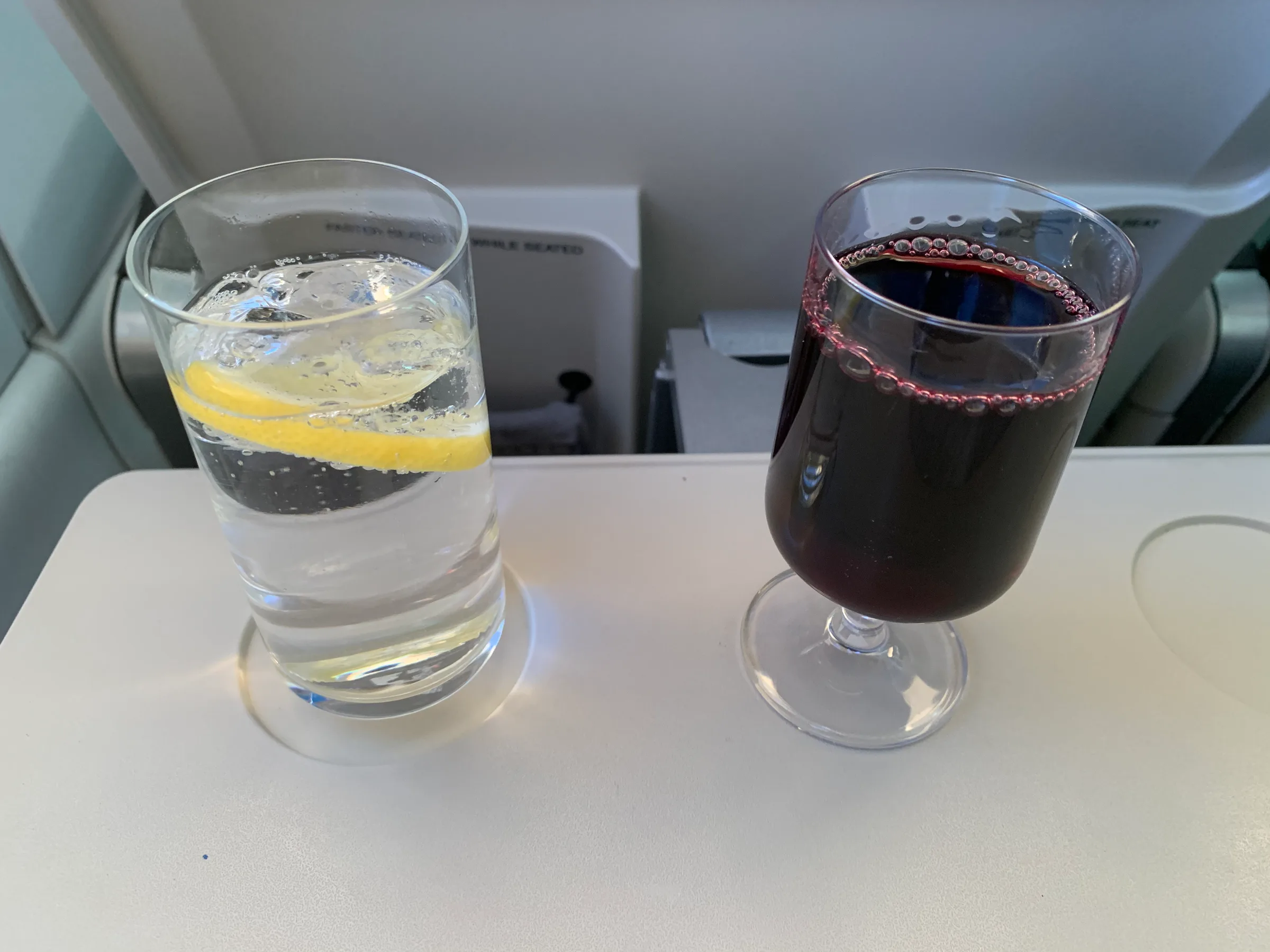 Glas Wasser mit Zitrone und Glas Rotwein auf Tisch im Flugzeug