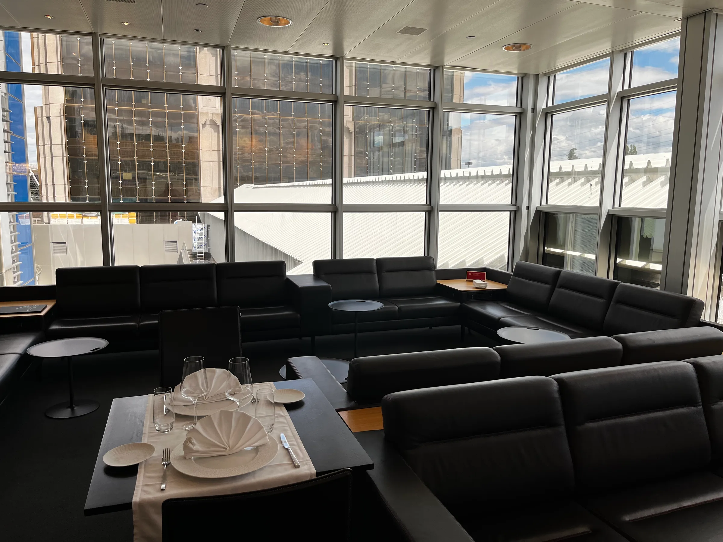 Lounge mit schwarzen Sofas und Tischen vor großen Fenstern