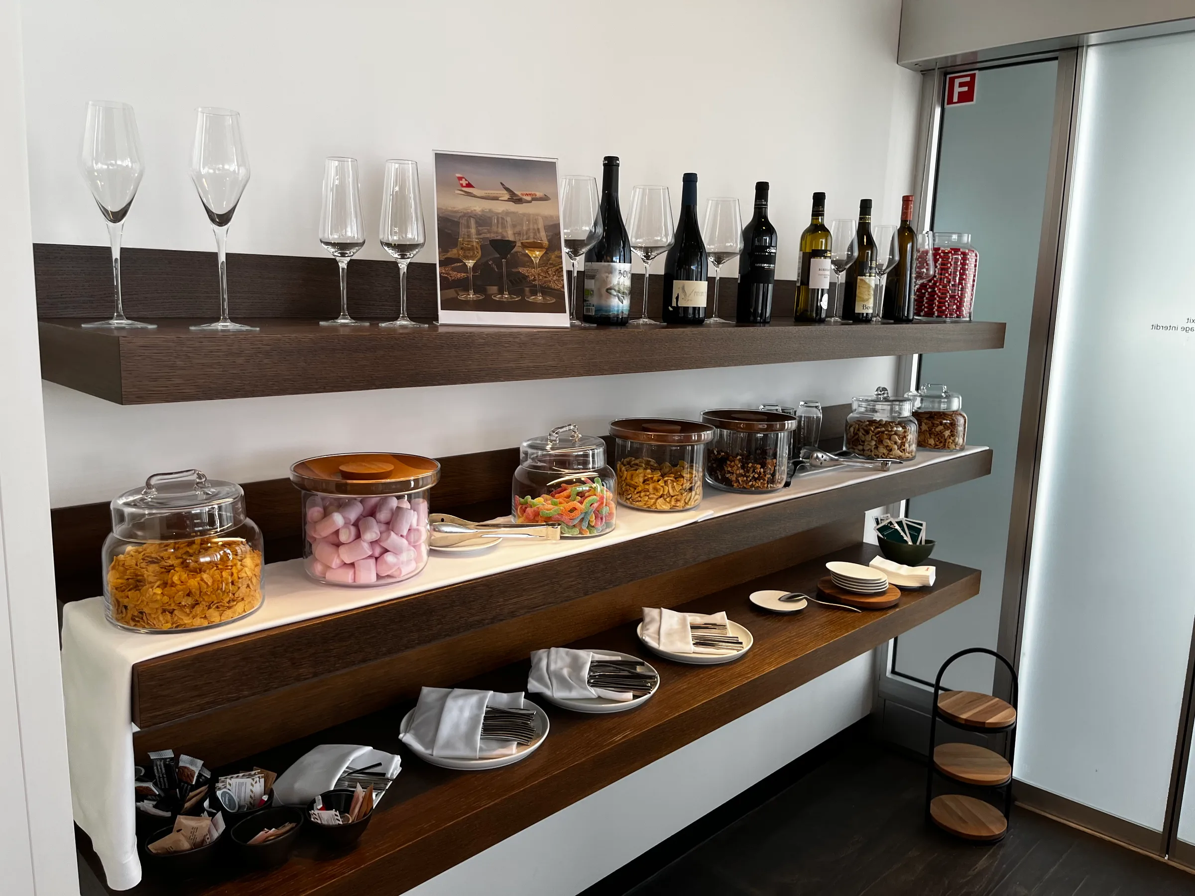 Lounge mit Weinflaschen, Gläsern und Snacks auf Holzregalen