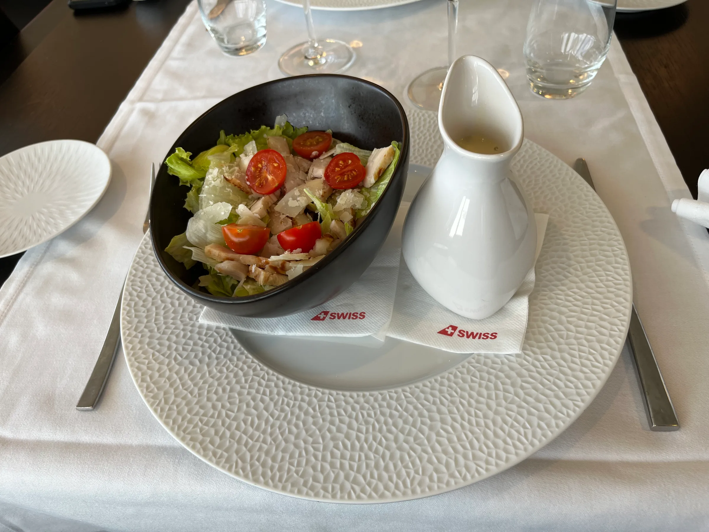 Salat mit Tomaten und Parmesan in einer schwarzen Schale auf einem weißen Teller mit SWISS-Logo