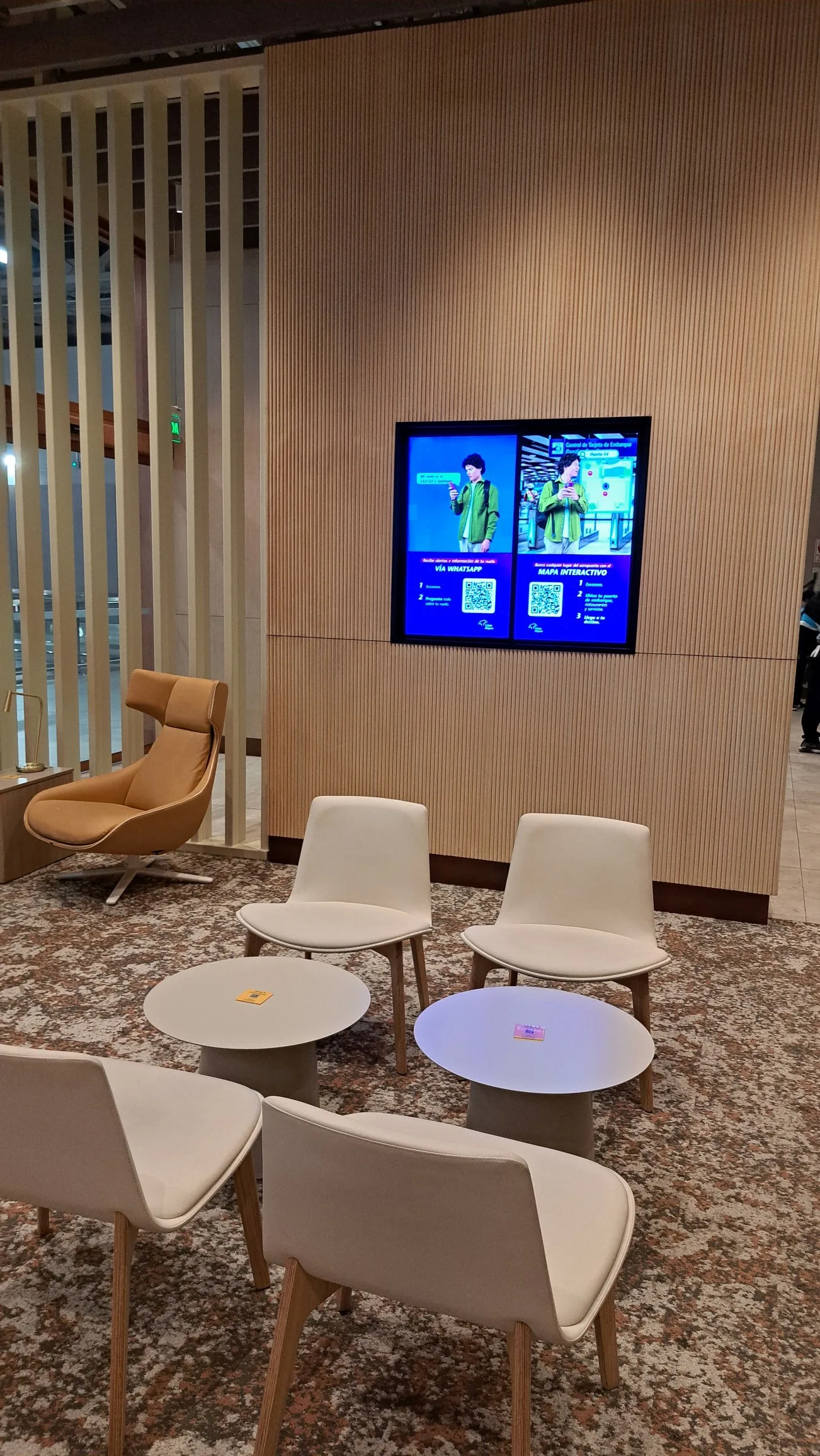 Lounge mit Sesseln und Couchtischen vor Holzwand mit Bildschirm