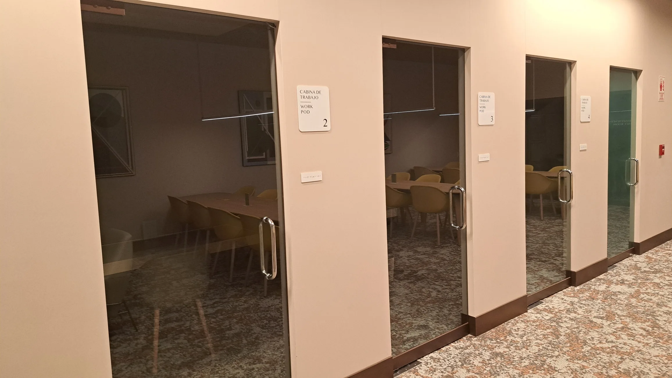 Glaswand vor Arbeitskabinen mit Sitzplätzen im Hintergrund