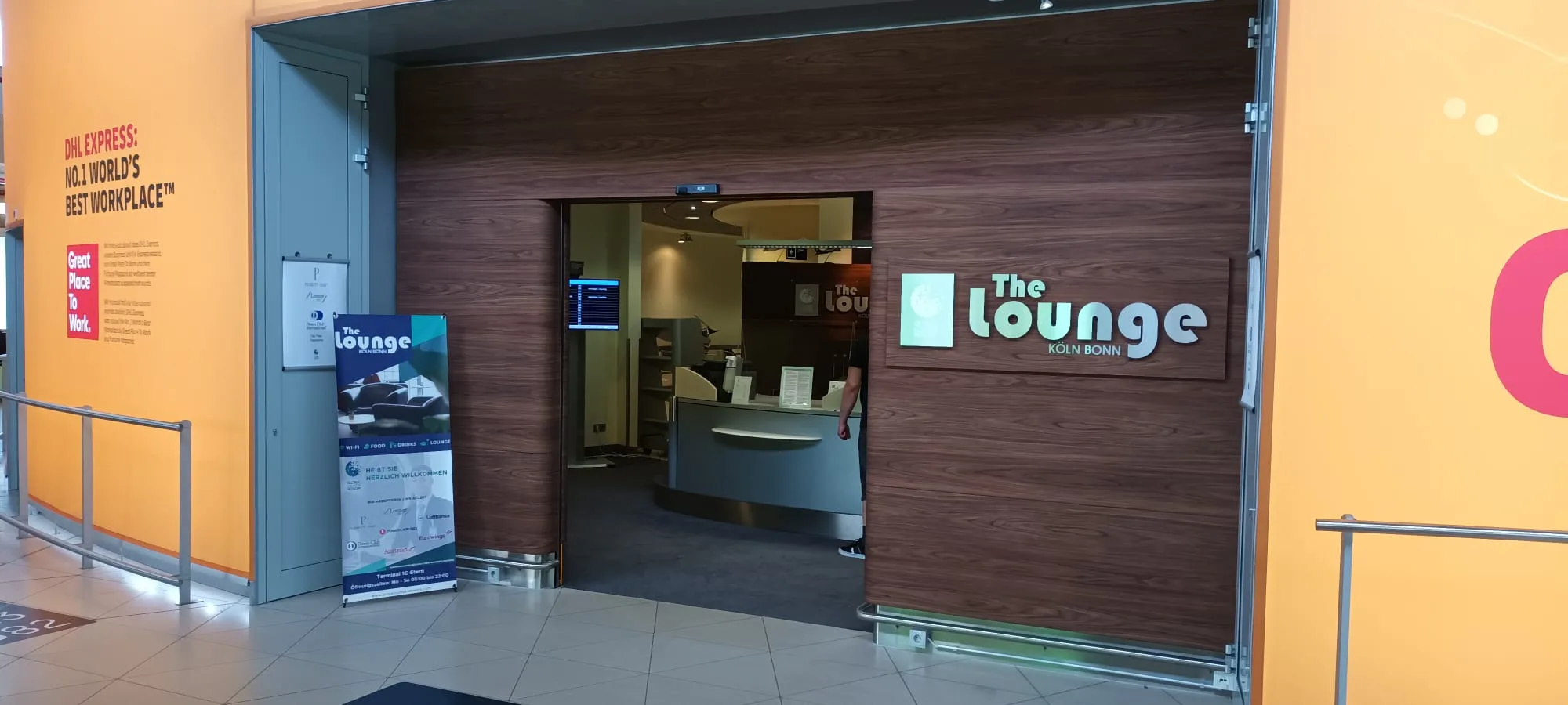 Eingang zur Lounge mit Holztür und Schild 'The lounge' am Flughafen Köln Bonn