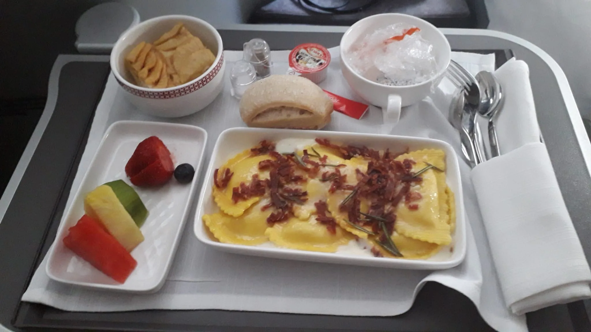 Gedeckter Flugzeugtisch mit Ravioli, Obst und Getränken