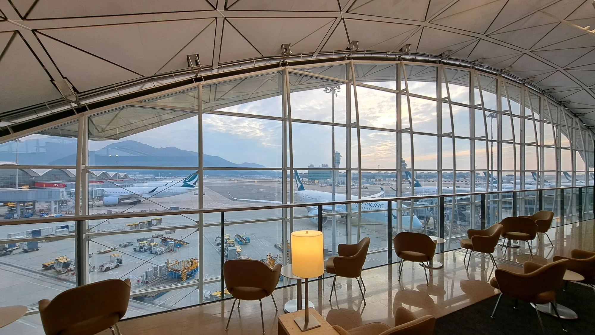 Lounge mit Sesseln und Tisch vor Panoramafenster mit Flugzeugen im Hintergrund