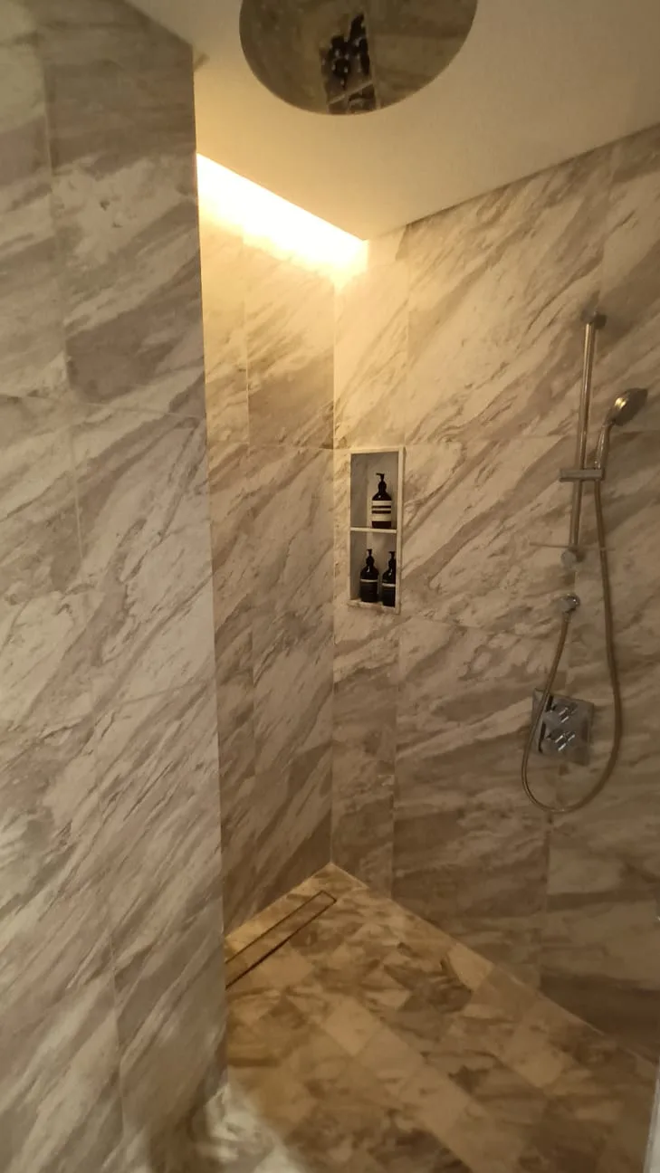 Dusche mit Marmorwänden und eingebautem Regal